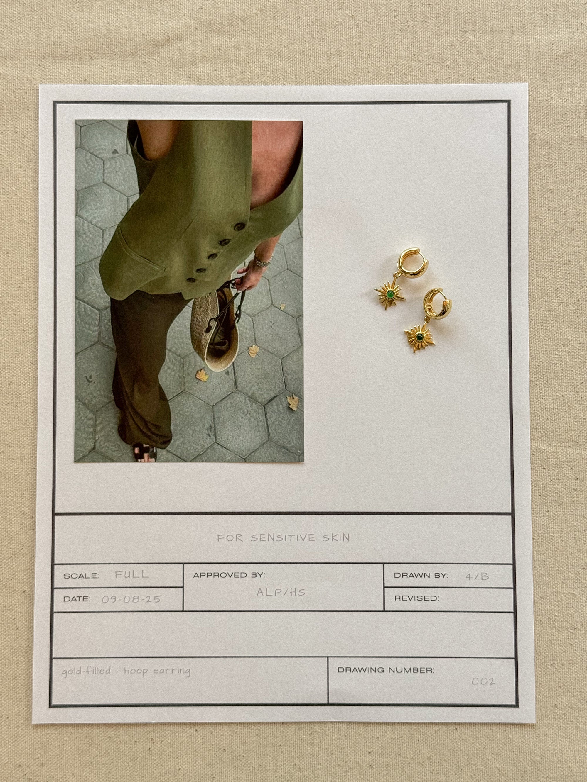 Gold earrings displayed on a card with a photo of a person wearing green pants.