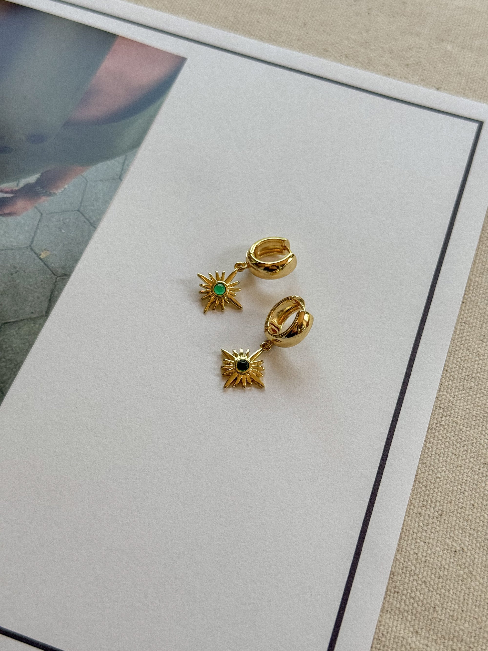 Gold earrings with green and black stones on a white card
