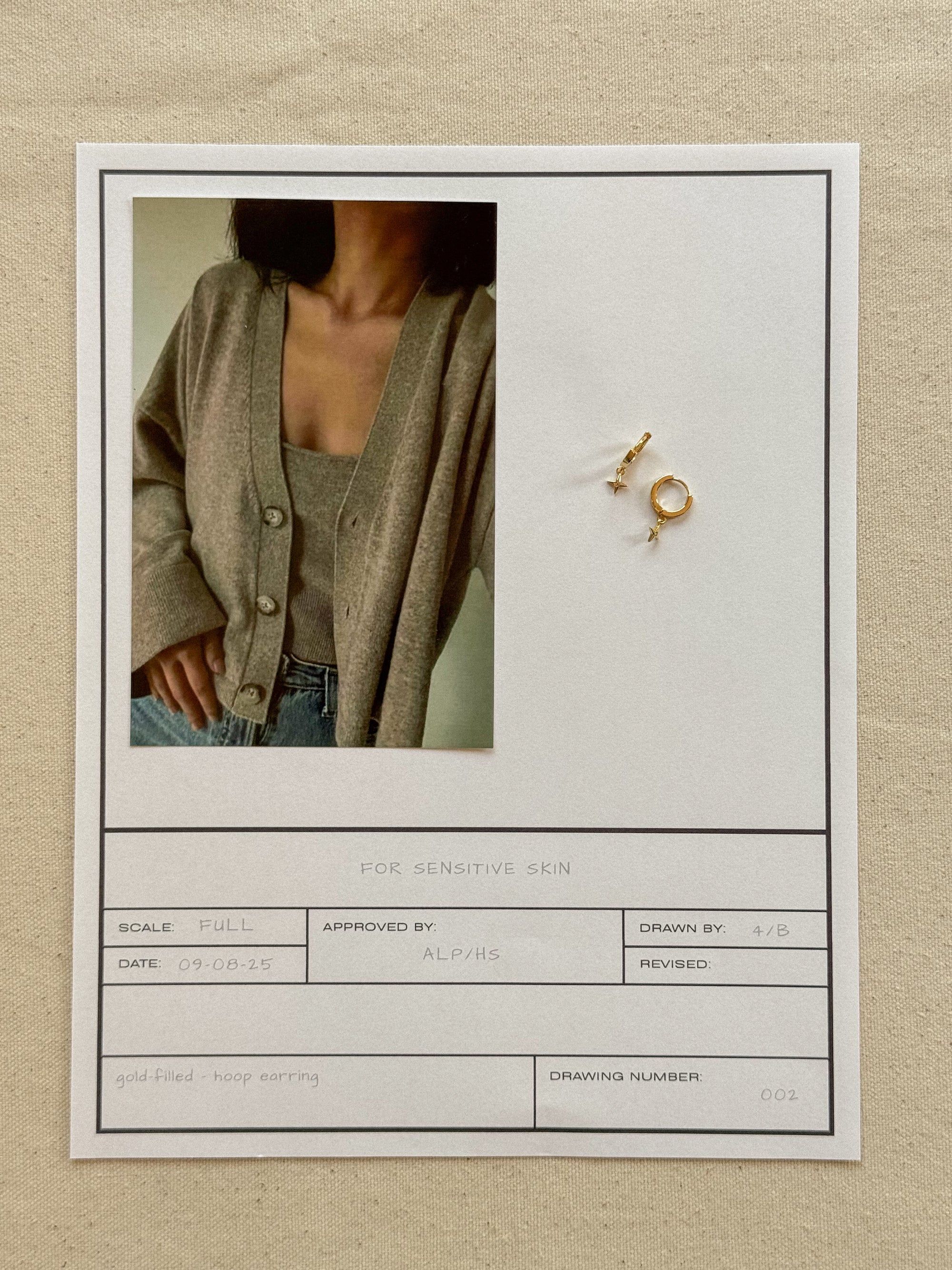 Earring displayed on a neutral background with a person wearing a cardigan.