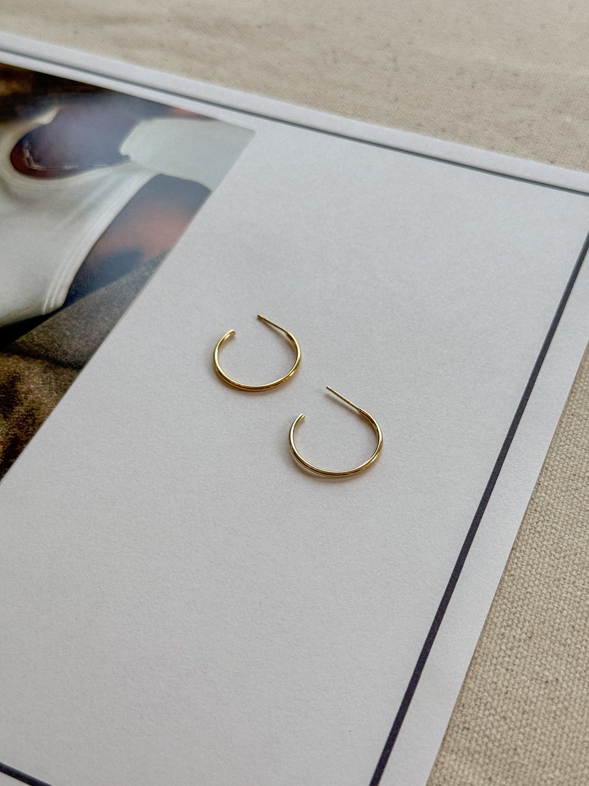 Gold hoop earrings on a white card with a blurred background
