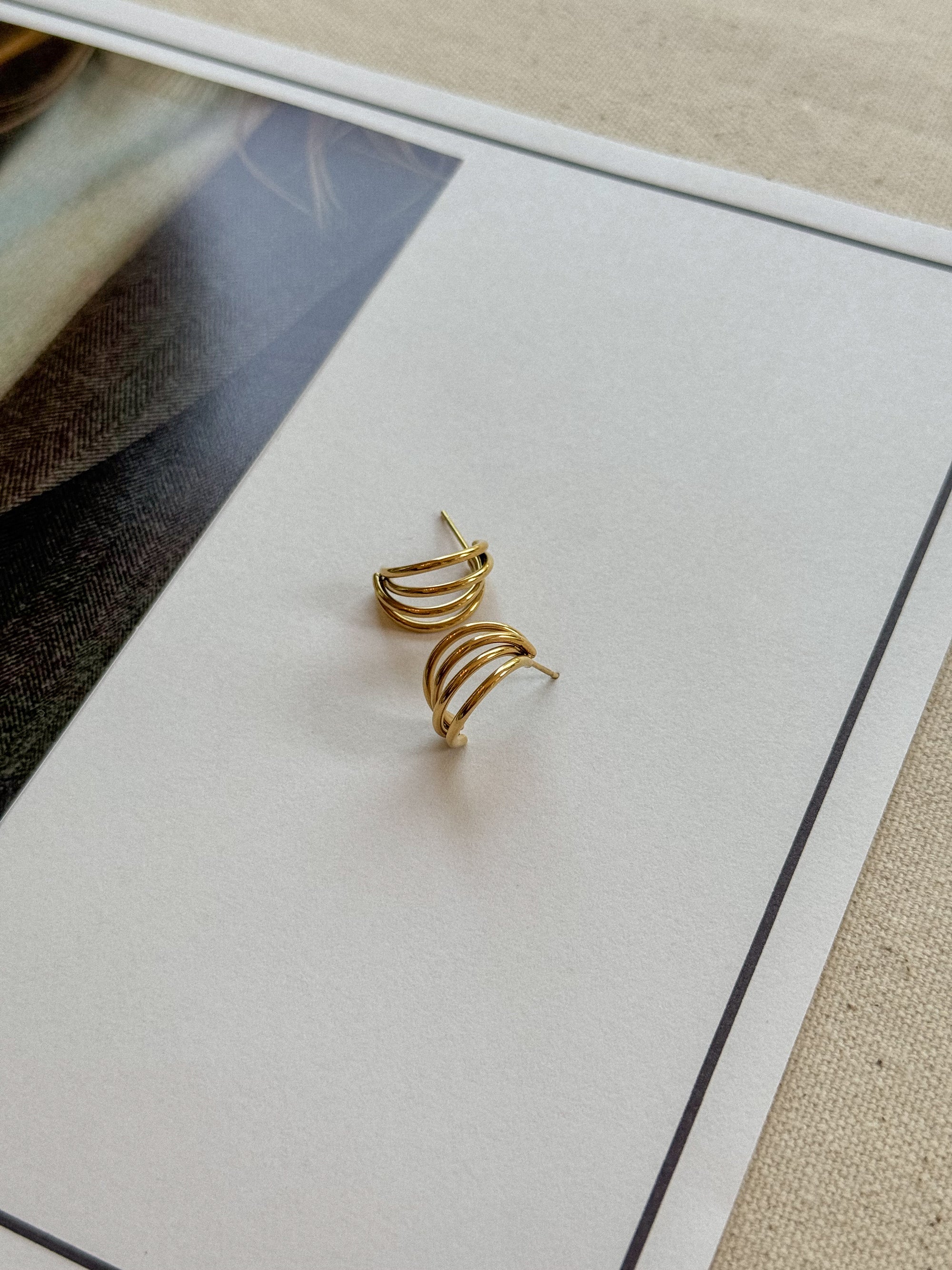 Gold earrings on a white card with a beige background