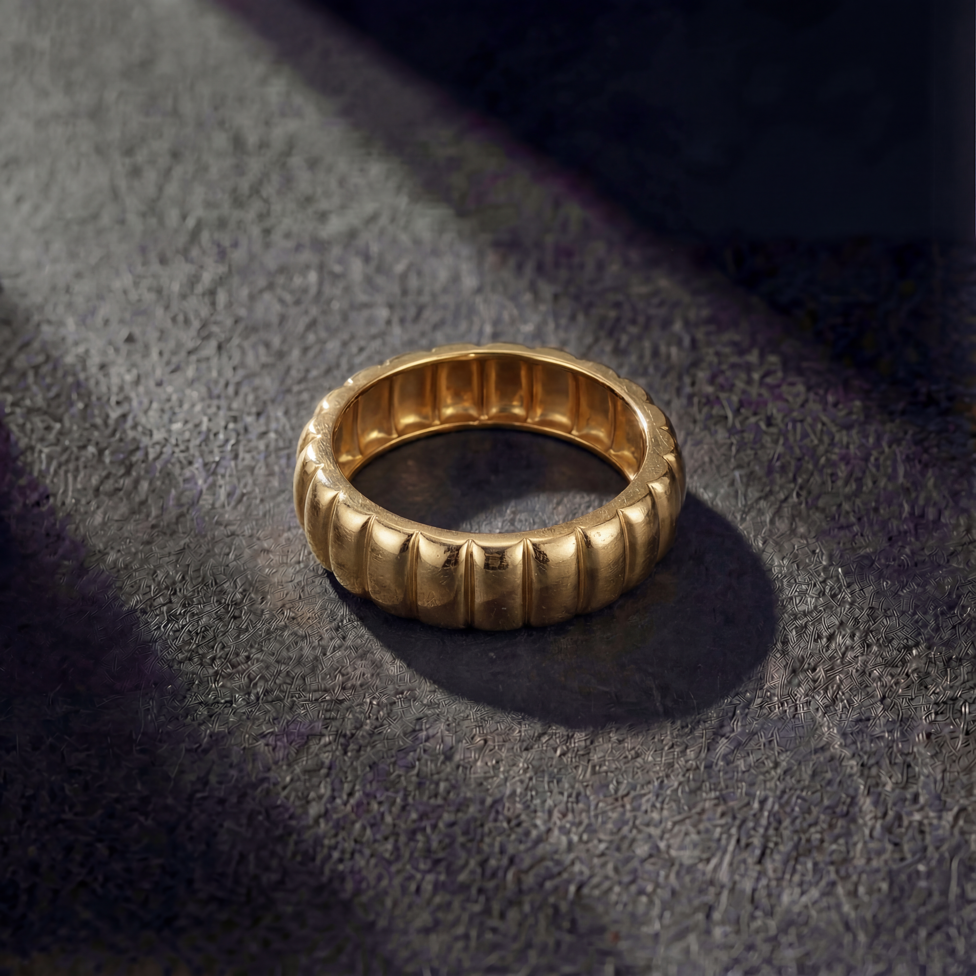 Gold ring with a ribbed design on a textured dark surface