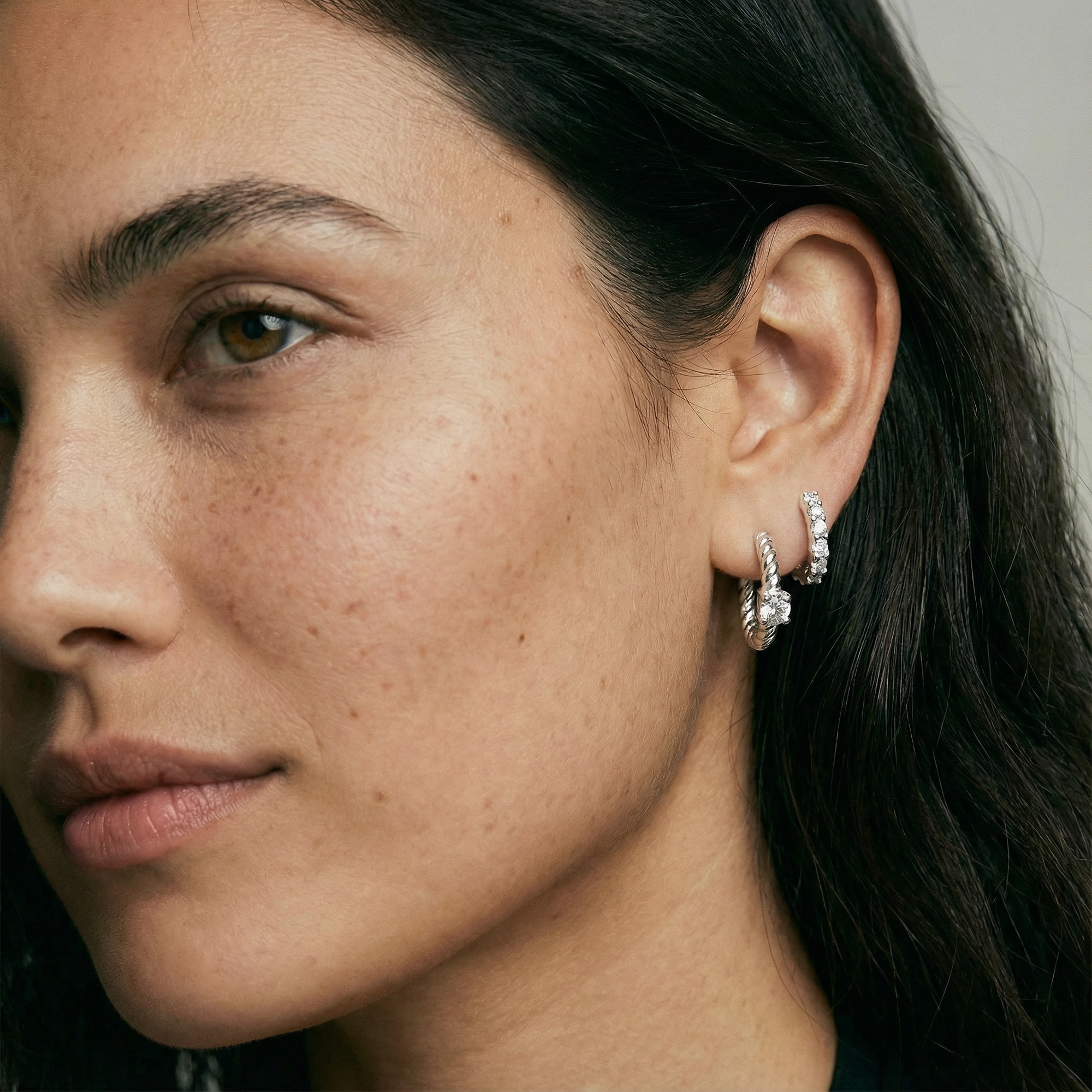 Close-up of a woman's face wearing silver hoop earrings with a neutral background