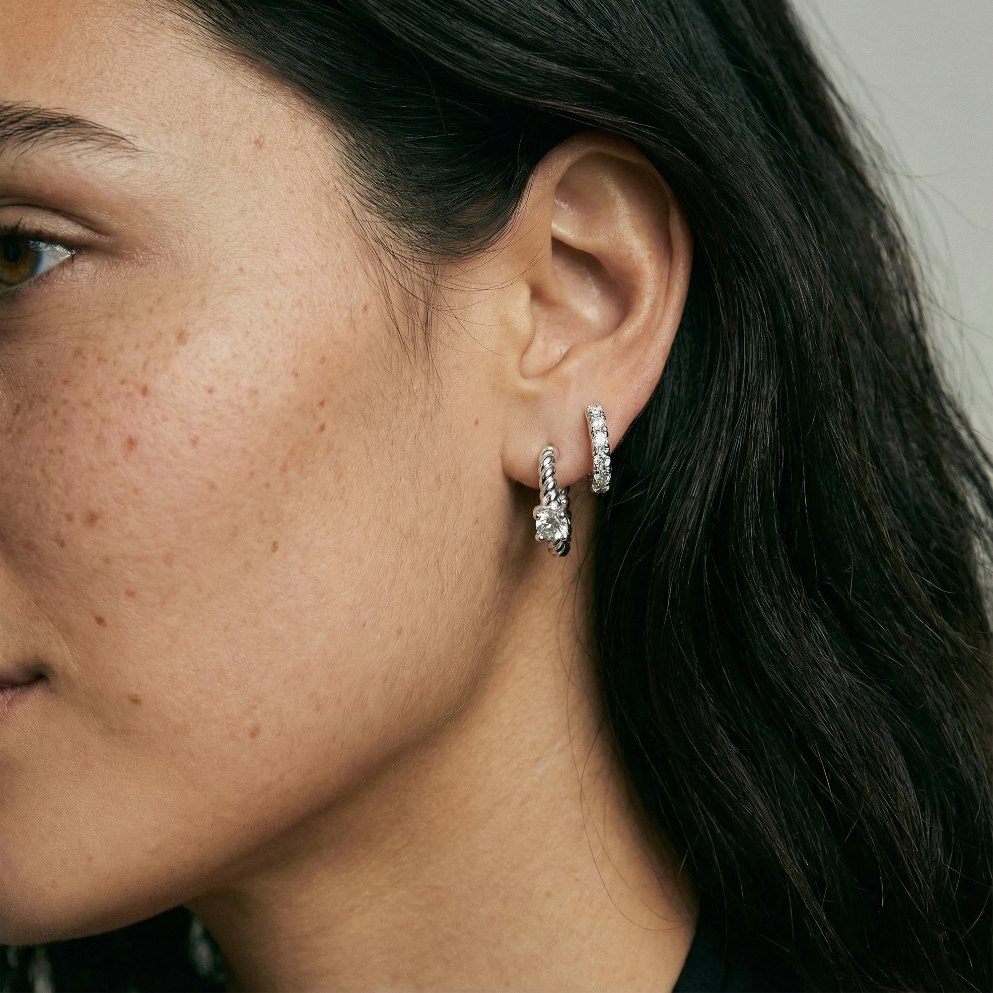 Close-up of a person wearing silver hoop earrings with a neutral background