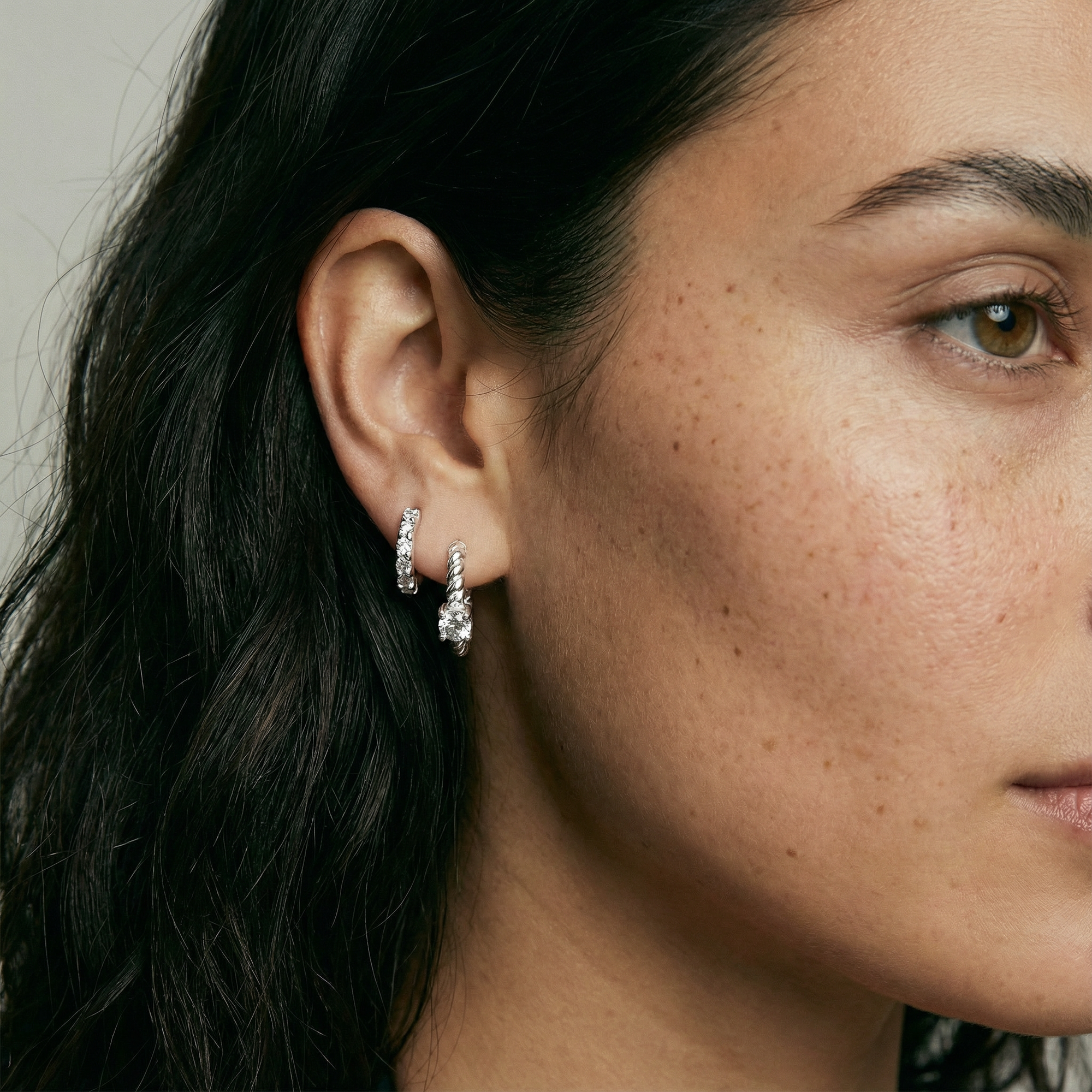 Close-up of a woman's ear wearing diamond earrings with a neutral background
