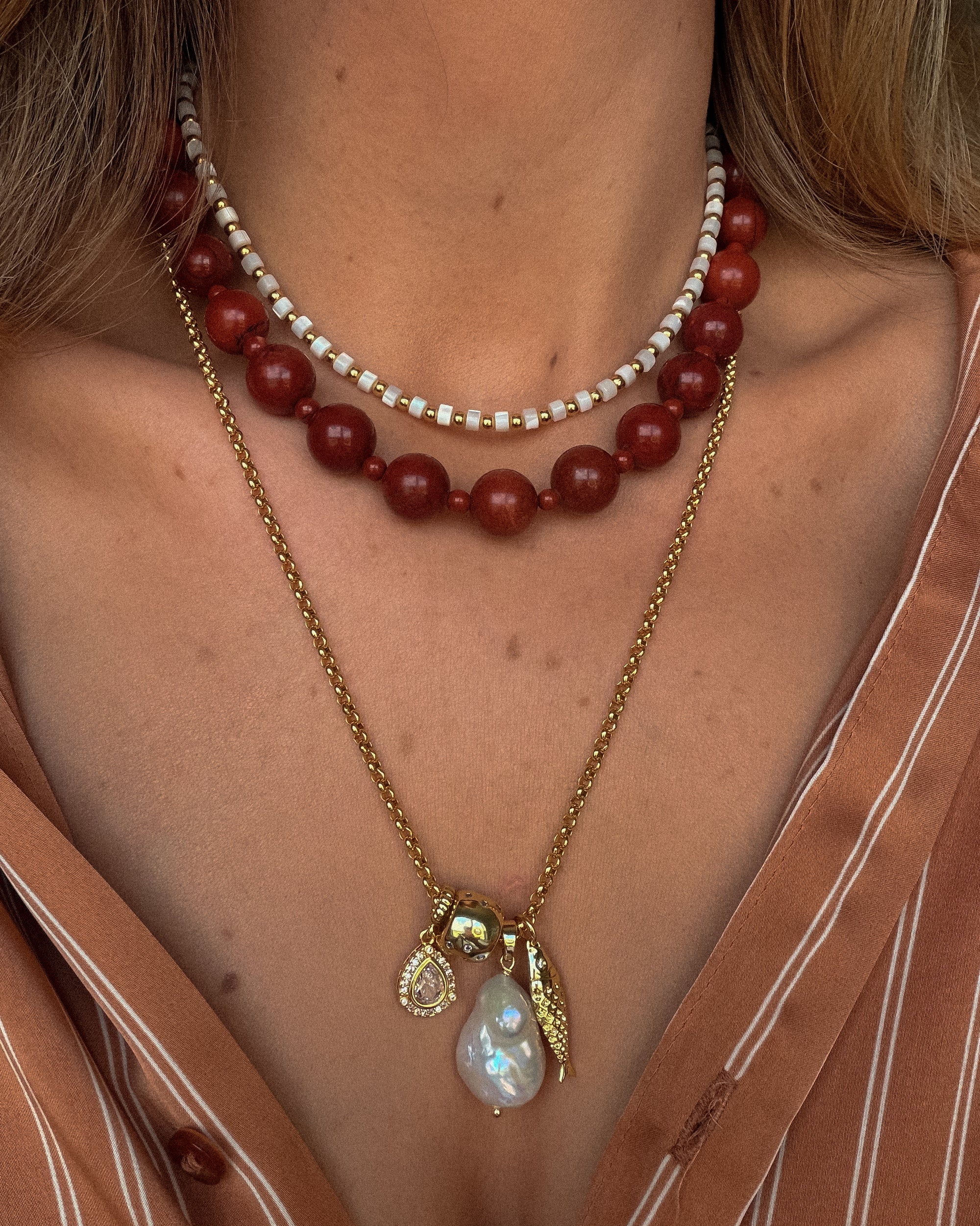 Close-up of a woman wearing a red beaded necklace and a gold chain with a pendant.