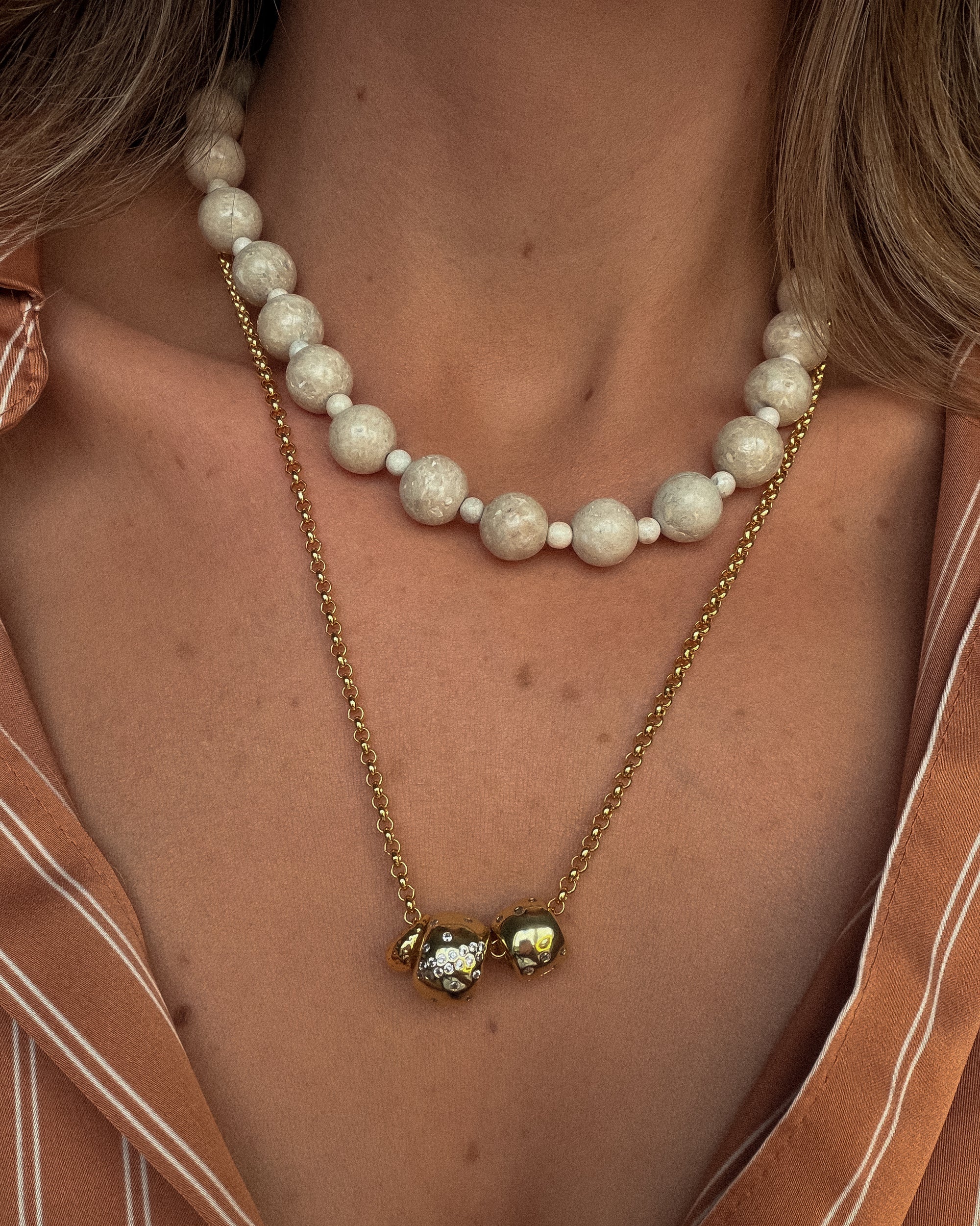 Pearl necklace with a gold chain and green gemstone pendant worn by a person.