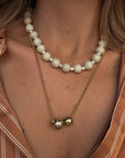 Pearl necklace with a gold chain and green gemstone pendant worn by a person.