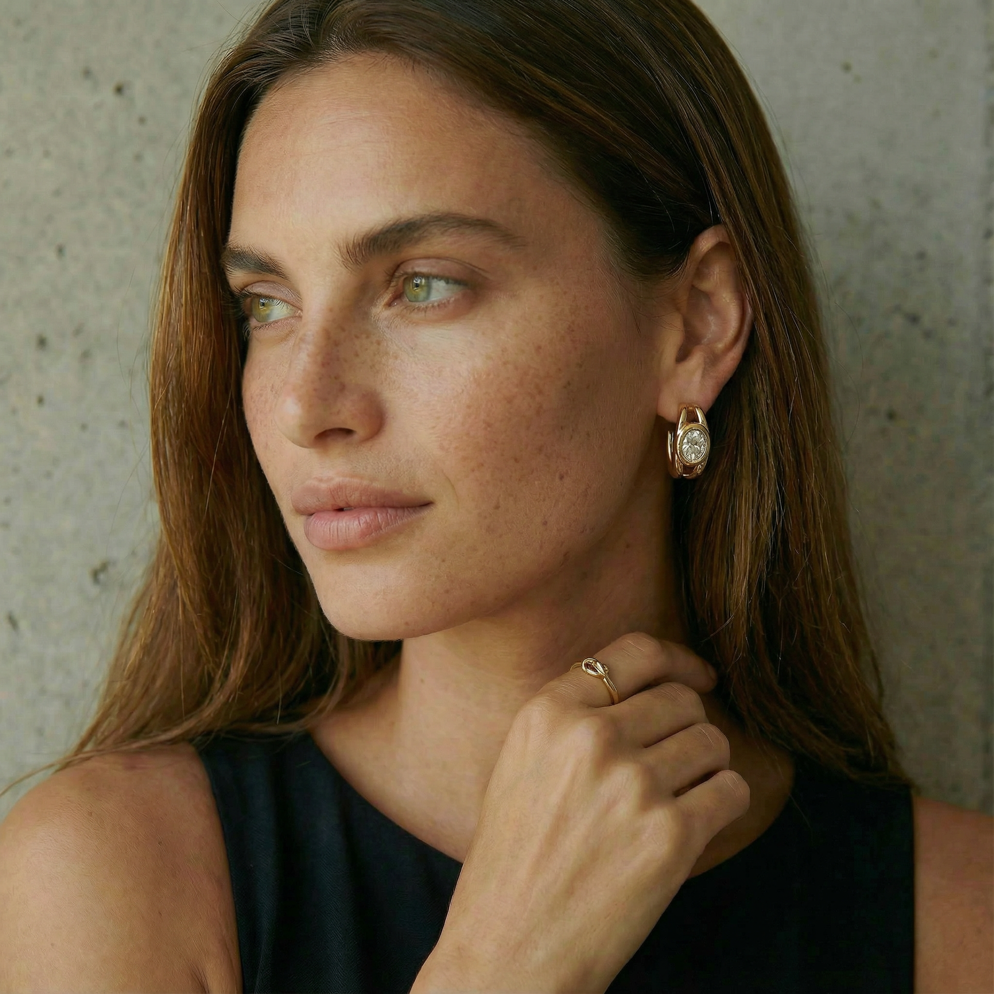 Woman wearing a gold earring and ring against a neutral background