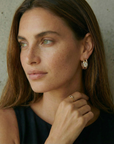 Woman wearing a gold earring and ring against a neutral background