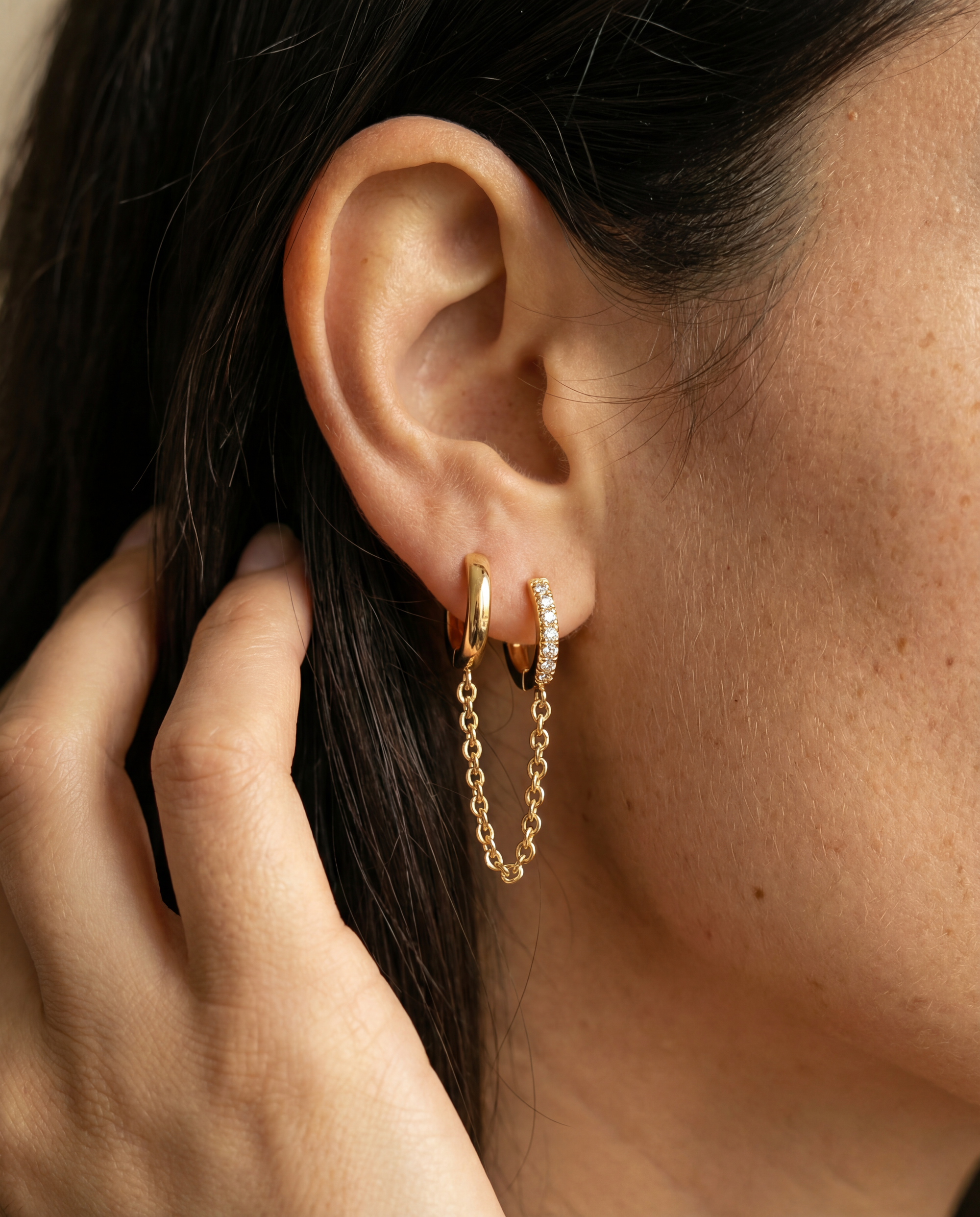 Close-up of an ear wearing gold hoop earrings with a hand adjusting hair.
