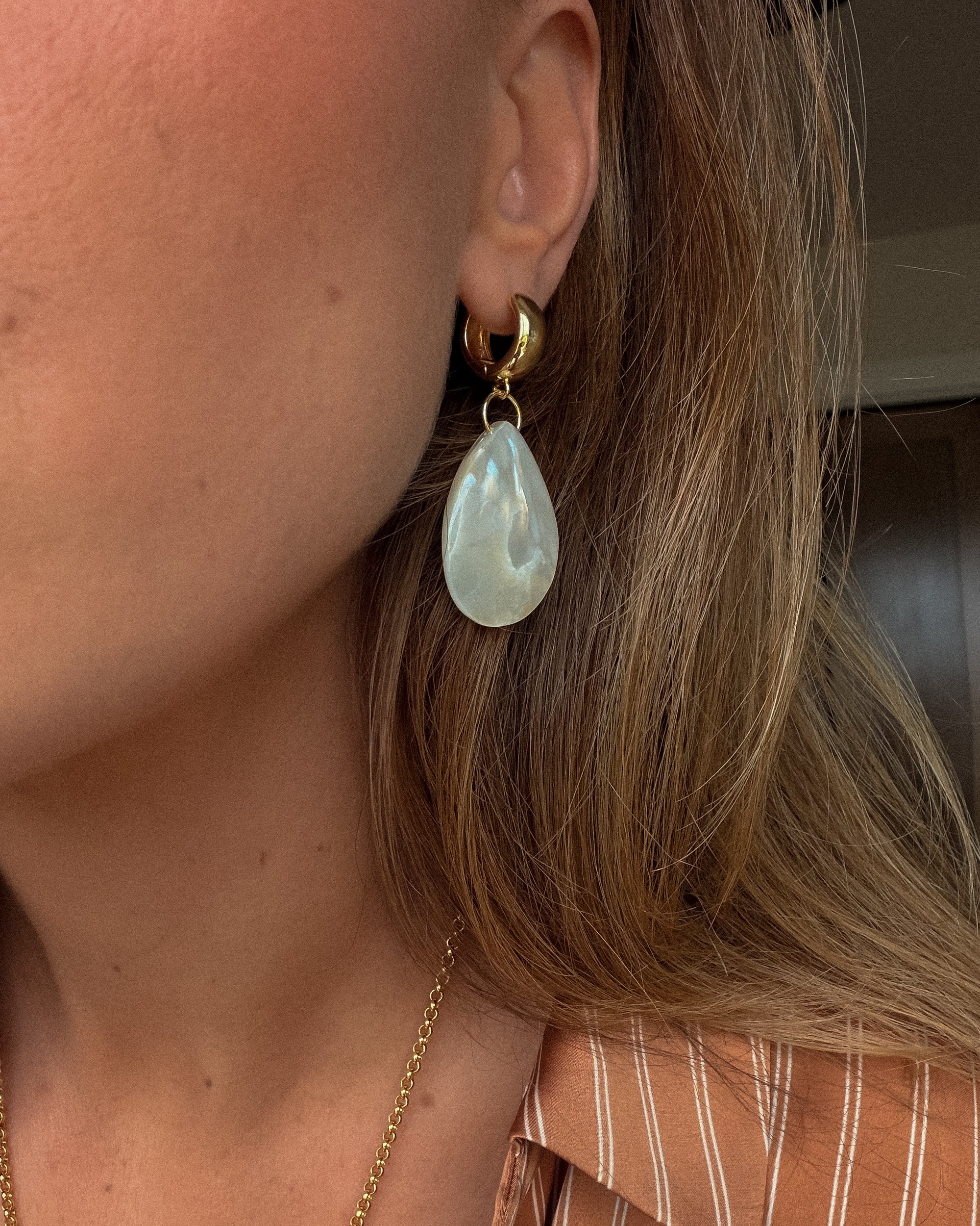Close-up of a person wearing a gold earring with a teardrop-shaped green gemstone.