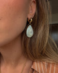 Close-up of a person wearing a gold earring with a teardrop-shaped green gemstone.