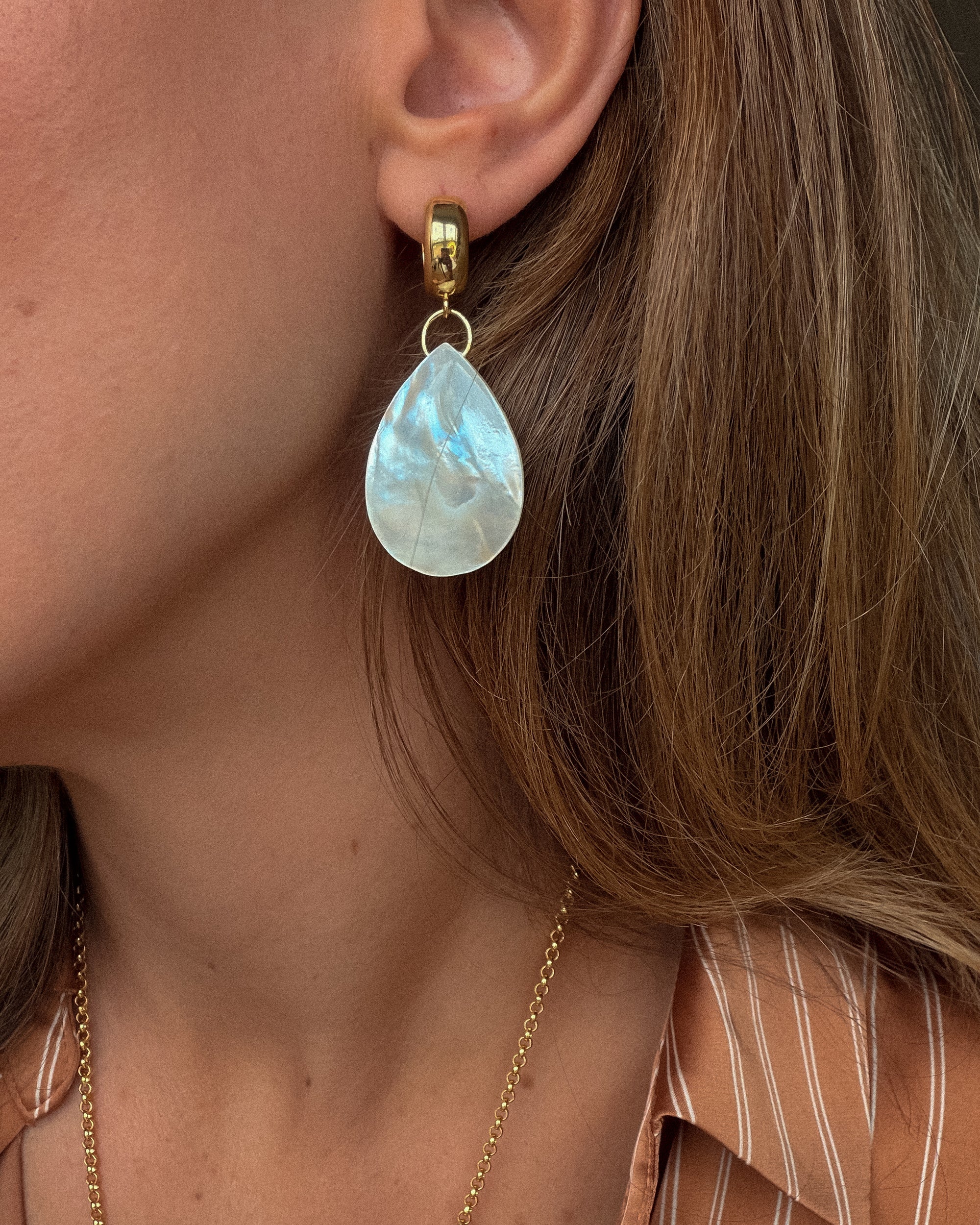 Close-up of a woman wearing a gold earring with a teardrop-shaped pearl-like stone.