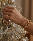 Hand wearing a gold bracelet on a Christmas tree with gold ornaments.