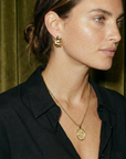 Woman wearing gold earrings and necklace against a green curtain background