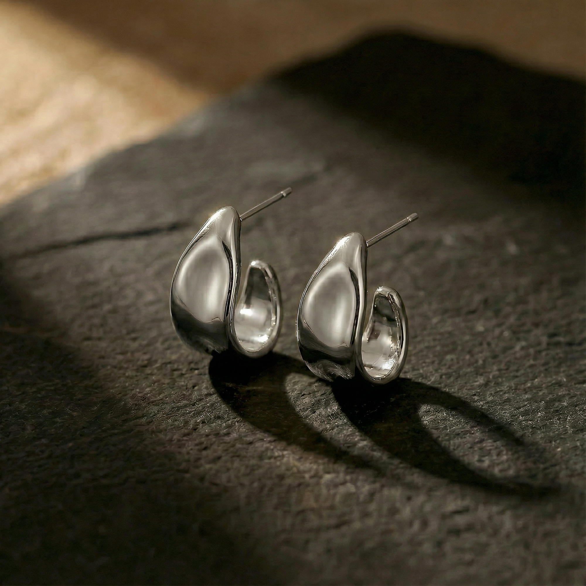 Pair of silver teardrop-shaped earrings on a dark surface