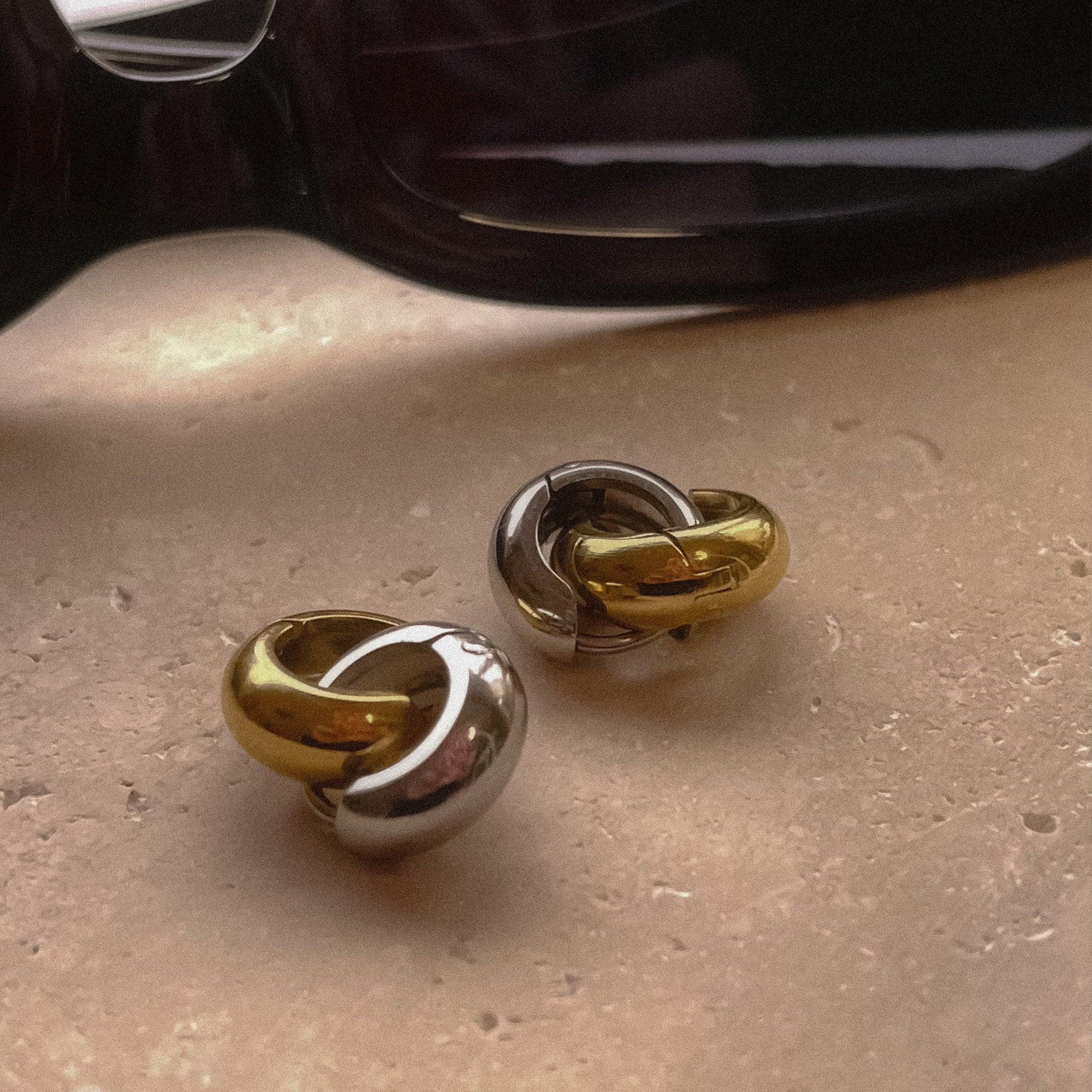 Photo of a shiny gold and shiny silver hoop earrings clasped together and sunglasses in the background.