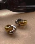 Photo of a shiny gold and shiny silver hoop earrings clasped together and sunglasses in the background.