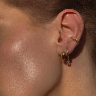 Close up of brunette and ear with a braided earring cuff, a teardrop hoop earring, and gold shiny huggie hoop earring.