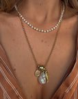 Close-up of a person wearing a gold necklace with a pendant featuring a pearl.