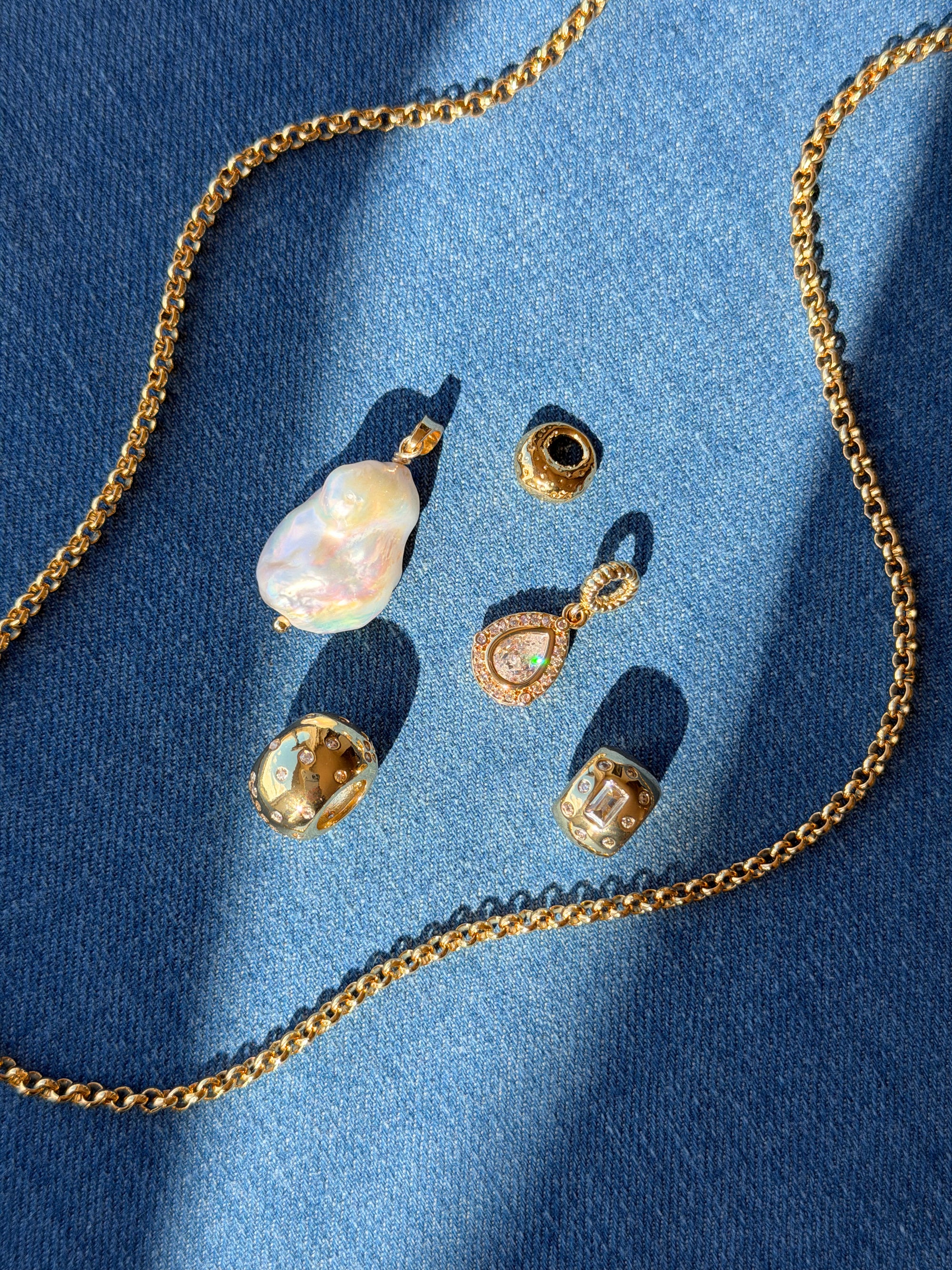 Gold jewelry set including necklace, earrings, and pendants on a blue fabric background