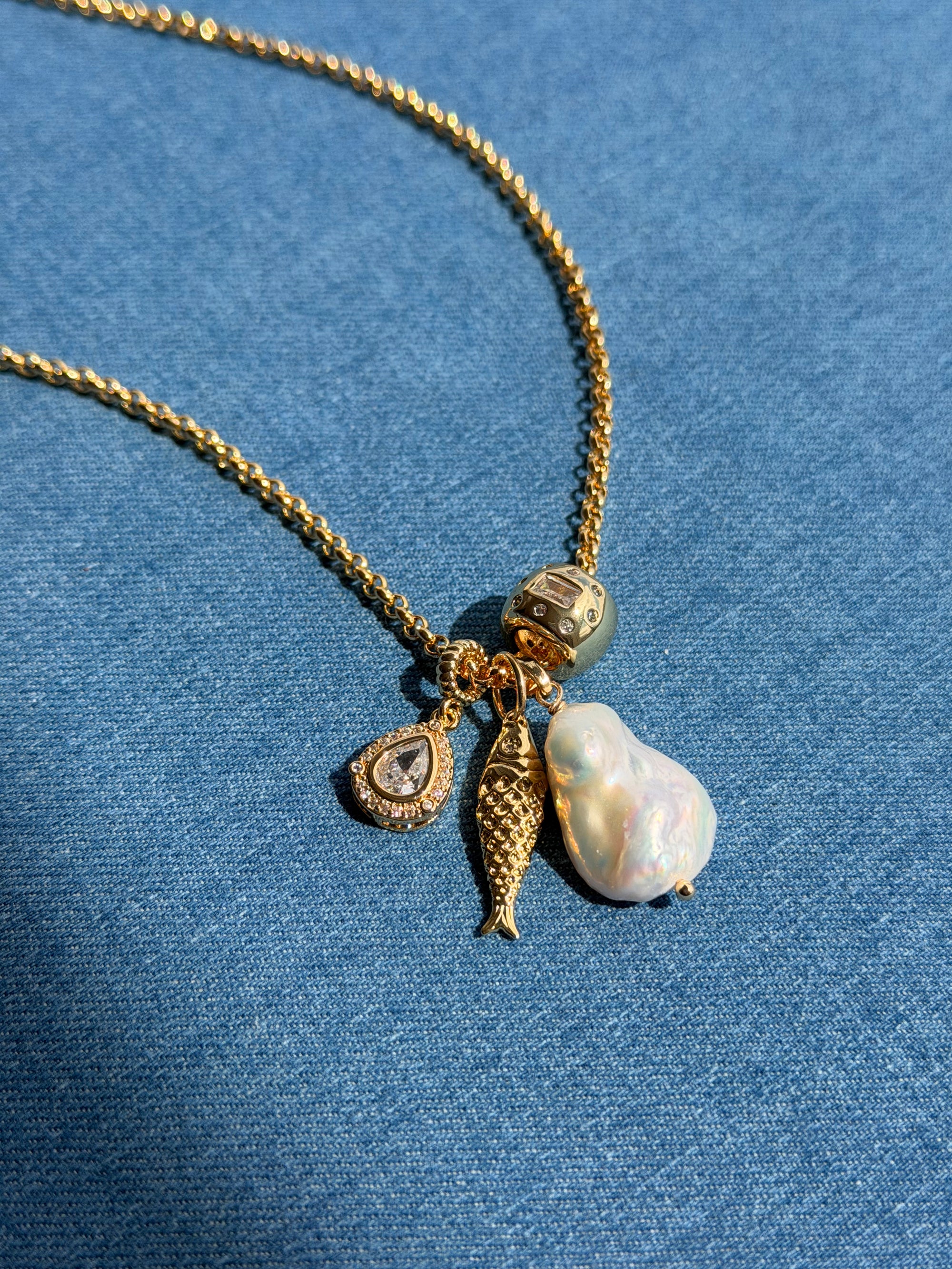 Gold necklace with various charms on a blue fabric background