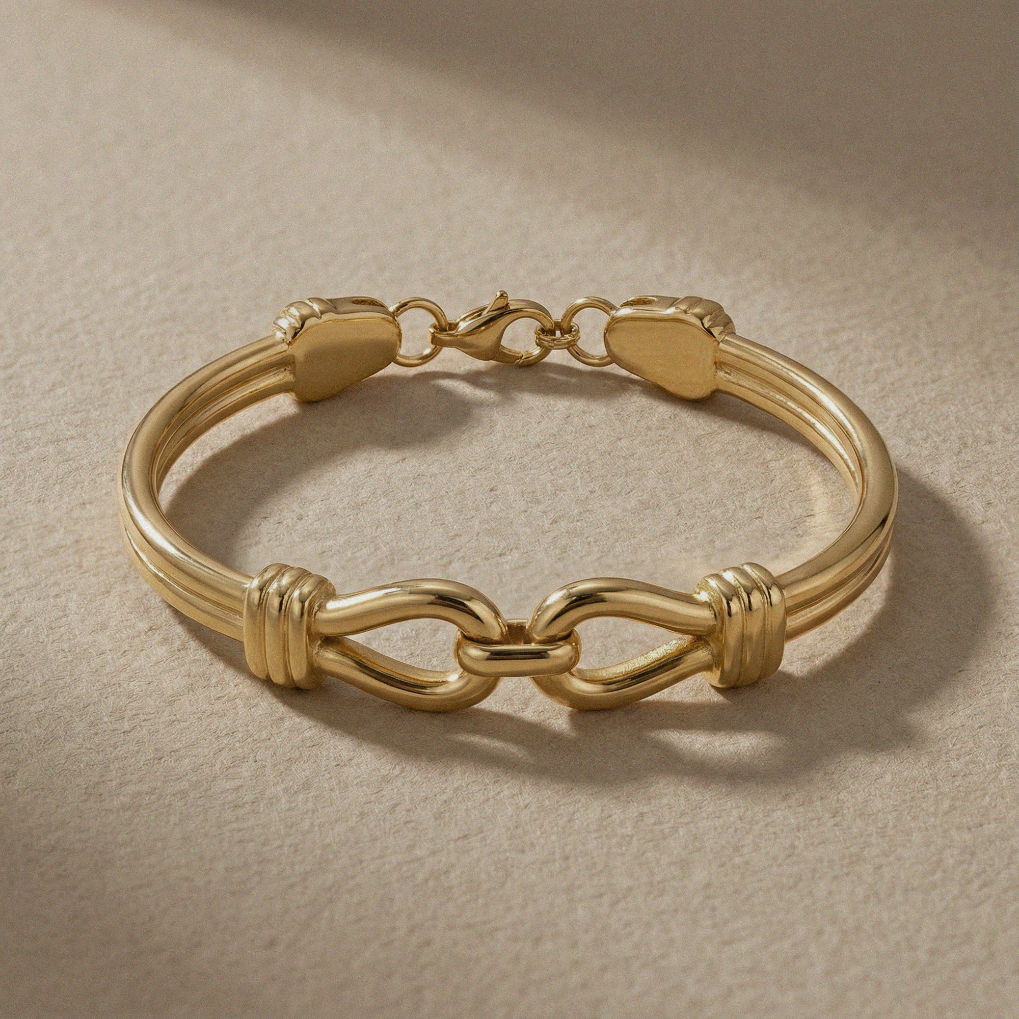 Gold bracelet with interlocking design on a beige background