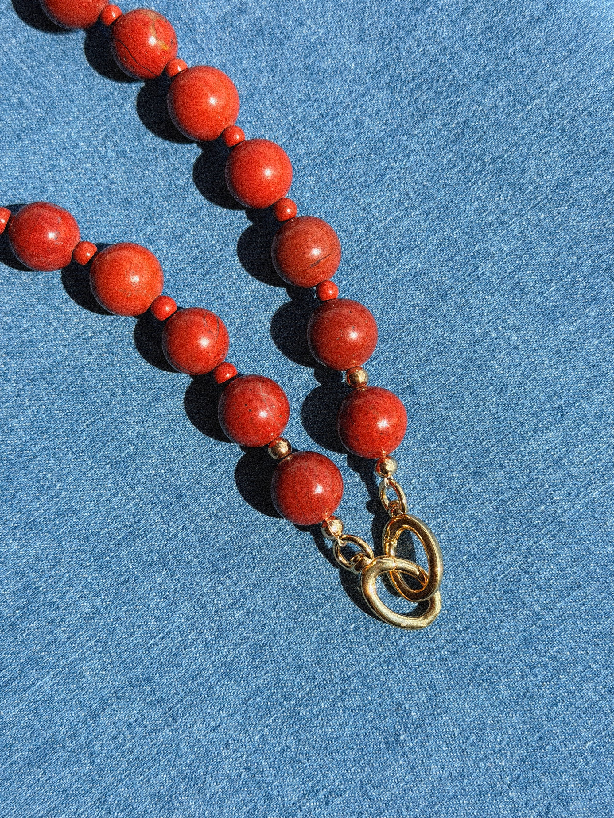 Red beaded necklace with a gold clasp on a blue fabric background