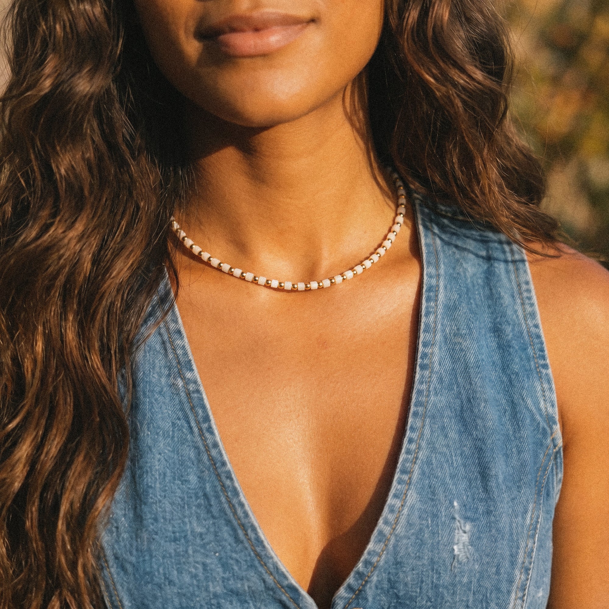 Woman wearing a denim vest and pearl necklace with a blurred natural background