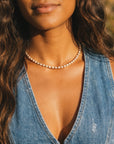 Woman wearing a denim vest and pearl necklace with a blurred natural background
