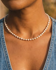 Person wearing a pearl necklace with a blurred background
