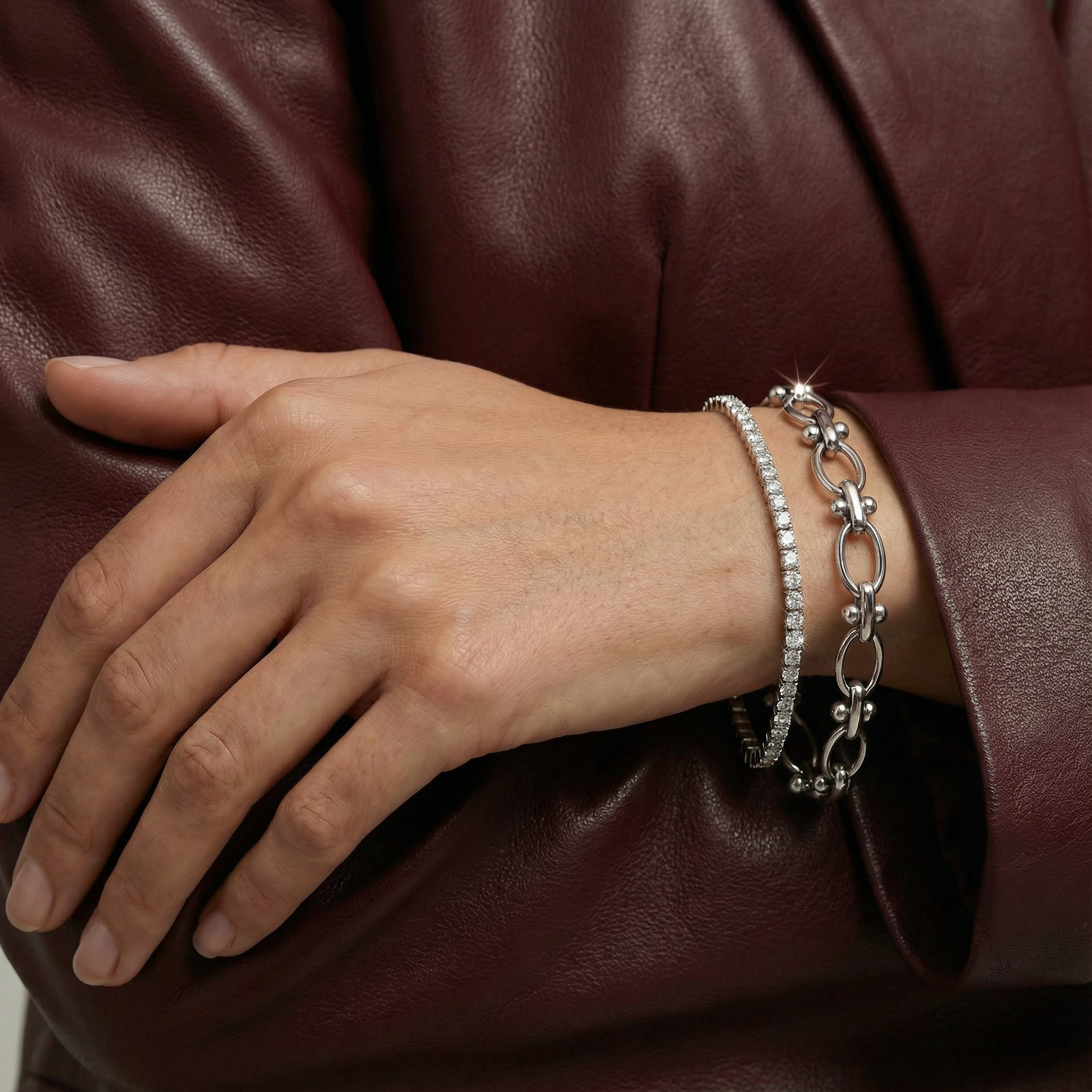 Hand wearing a silver bracelet on a person in a maroon leather jacket.