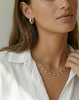 Woman wearing a gold necklace and earrings against a neutral background