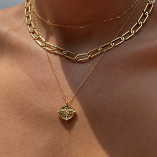 Sun soaked female chest with three gold necklaces. One necklace is a coin layering chain, another one is a bold link chain and the last is a dainty link chain with cubic zirconia.