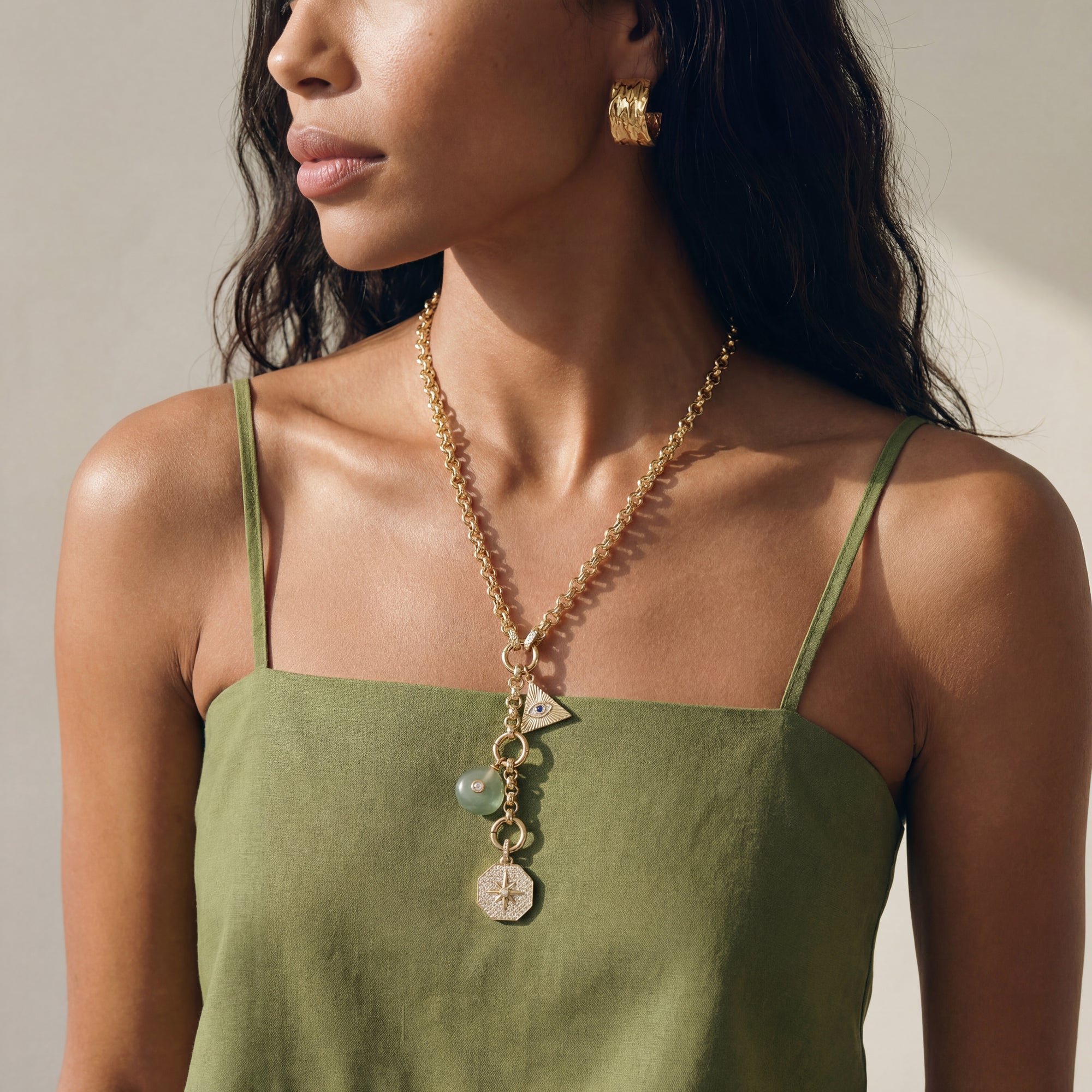 Woman wearing a green dress and gold necklace with pendant against a neutral background