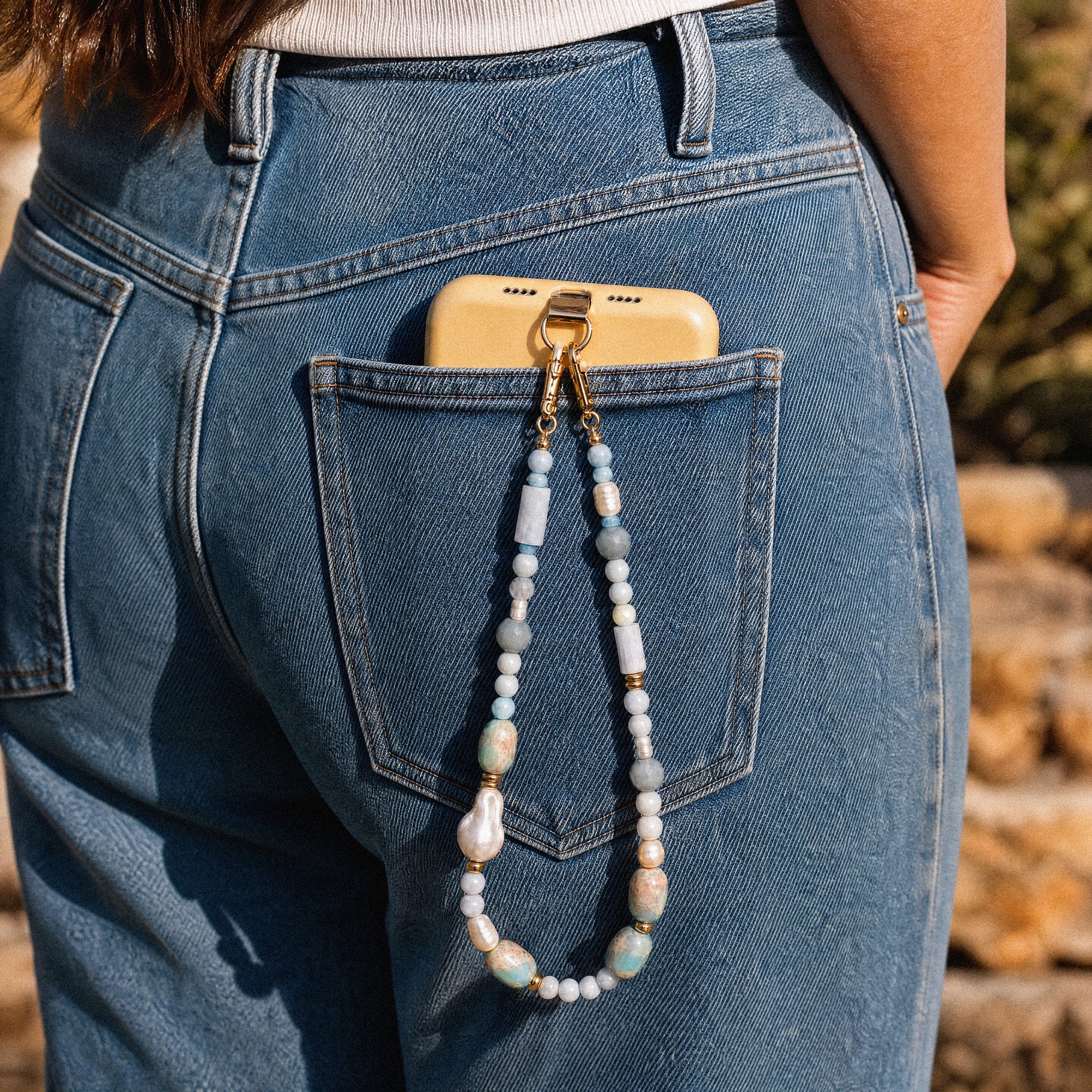 Person wearing blue jeans with a phone case and necklace hanging out of the pocket.