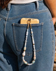 Person wearing blue jeans with a phone case and necklace hanging out of the pocket.