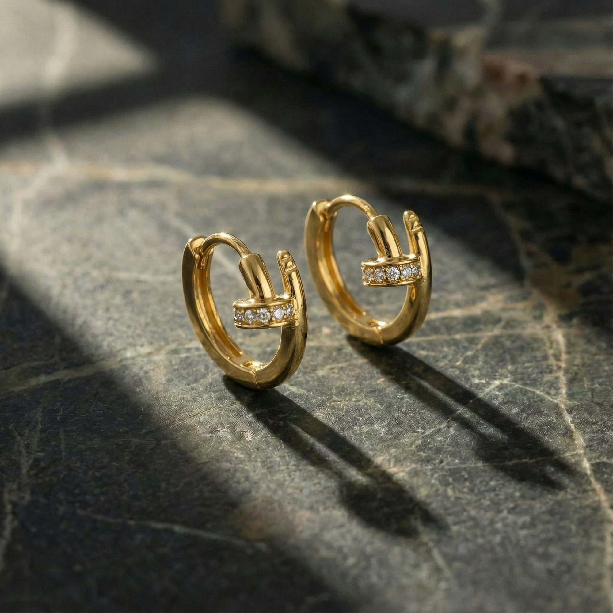Gold hoop earrings with embedded stones on a dark stone surface