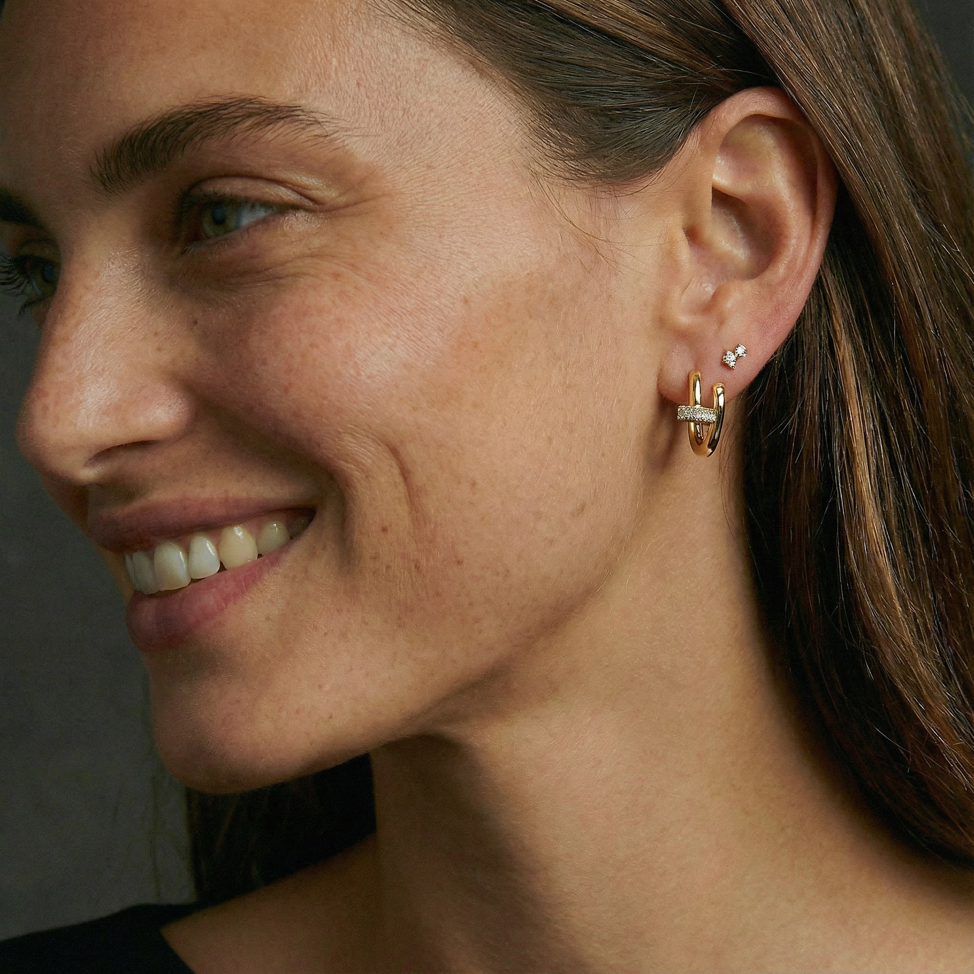Close-up of a woman wearing gold hoop earrings with a dark background