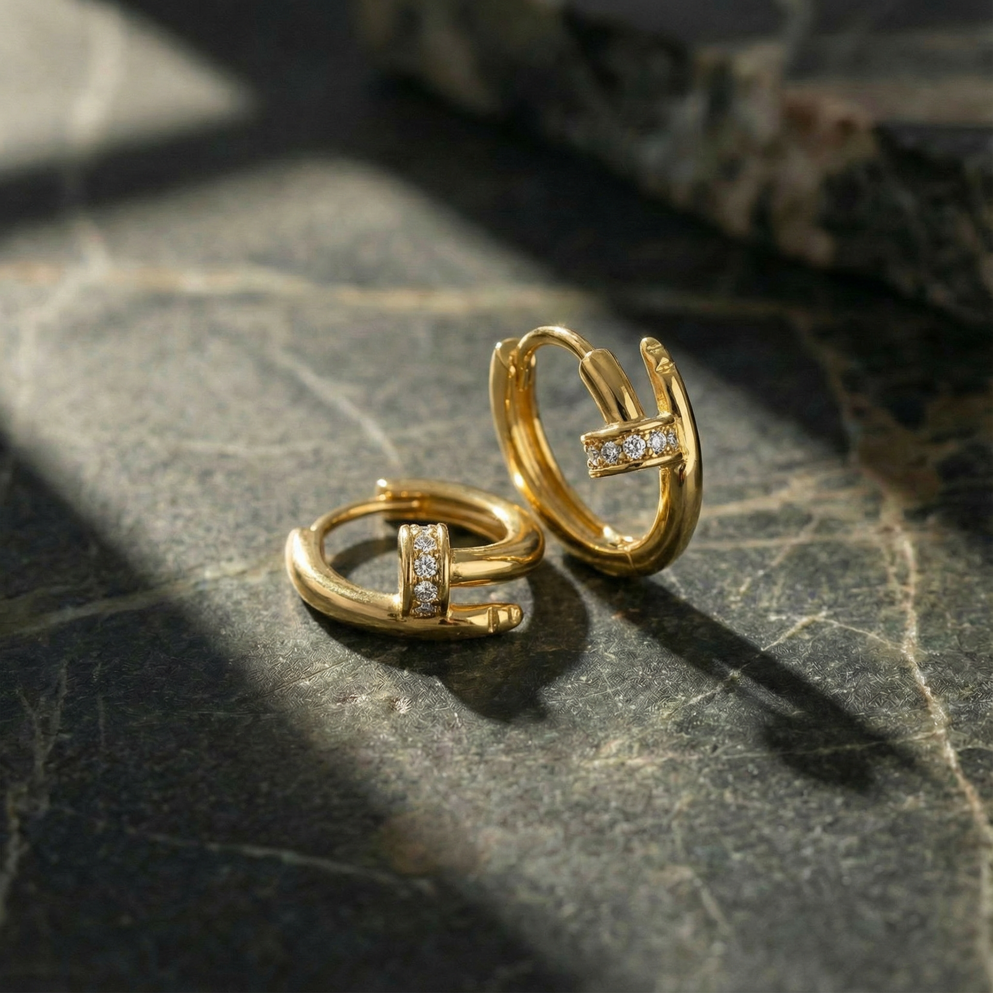 Gold hoop earrings with embedded stones on a dark stone surface