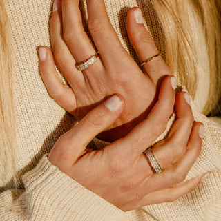 Two hands holding one another with three gold stacking rings. All rings have diamonds and are promoting hoftstudio.com